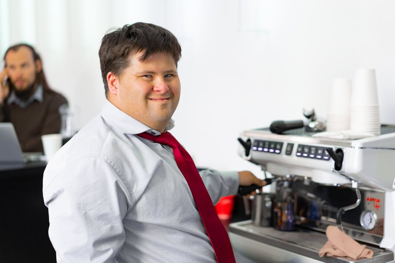 Man with Down syndrome smiling while making coffee at a cafe, symbolizing inclusivity.
